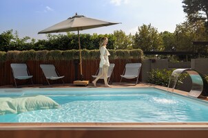 Piscina con fuente de agua, rodeada de sillones de descanso y una valla de madera.