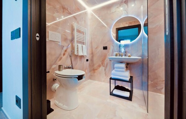 A modern bathroom with a marble floor, a white toilet, a sink with a mirror, and a towel rack. - BOUTIQUE HOTEL SIRMIONE (Sirmione)