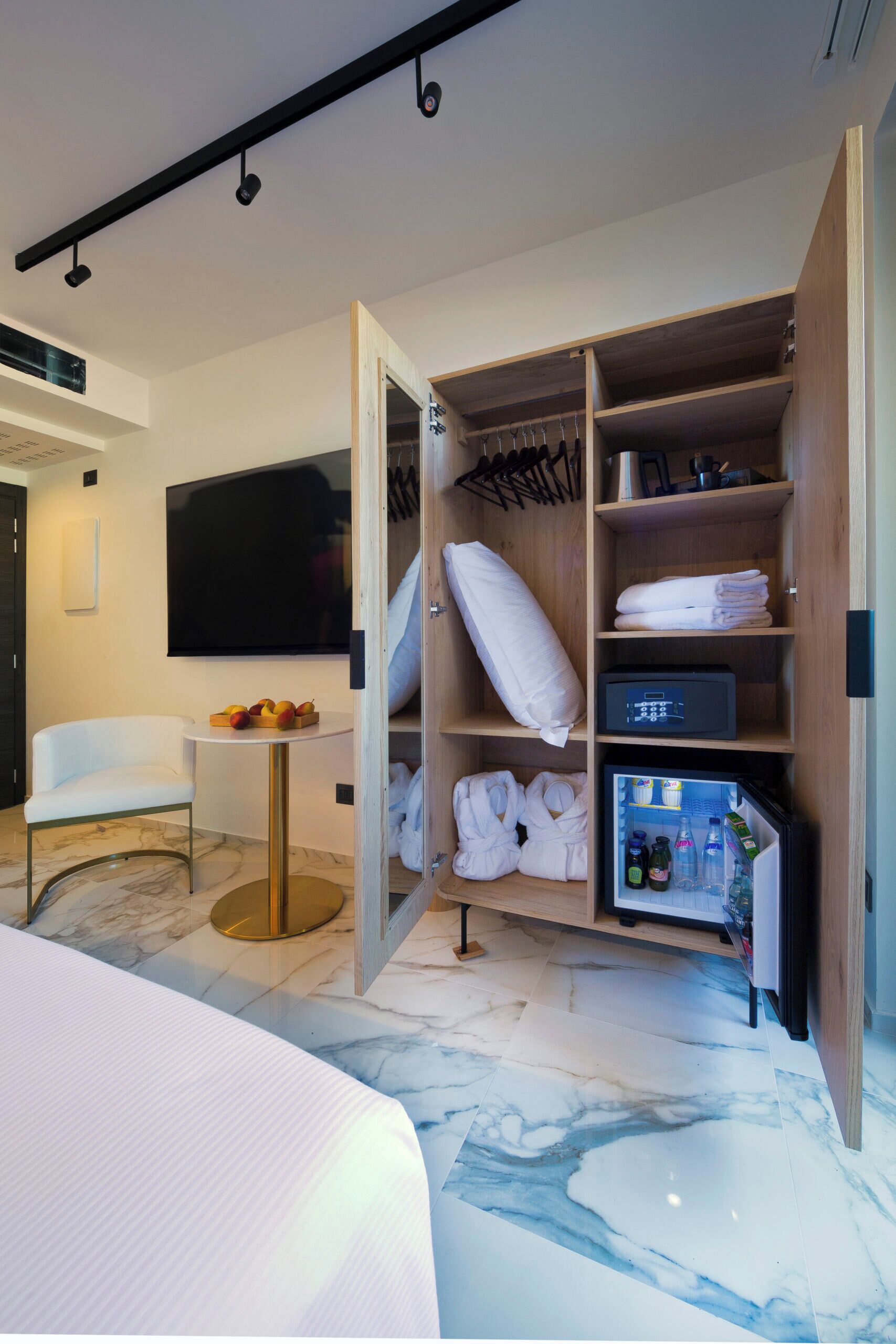 Quarto de hotel com um guarda-roupa bem arrumado, um espaço de estar confortável e uma pequena mesa com fruta.
