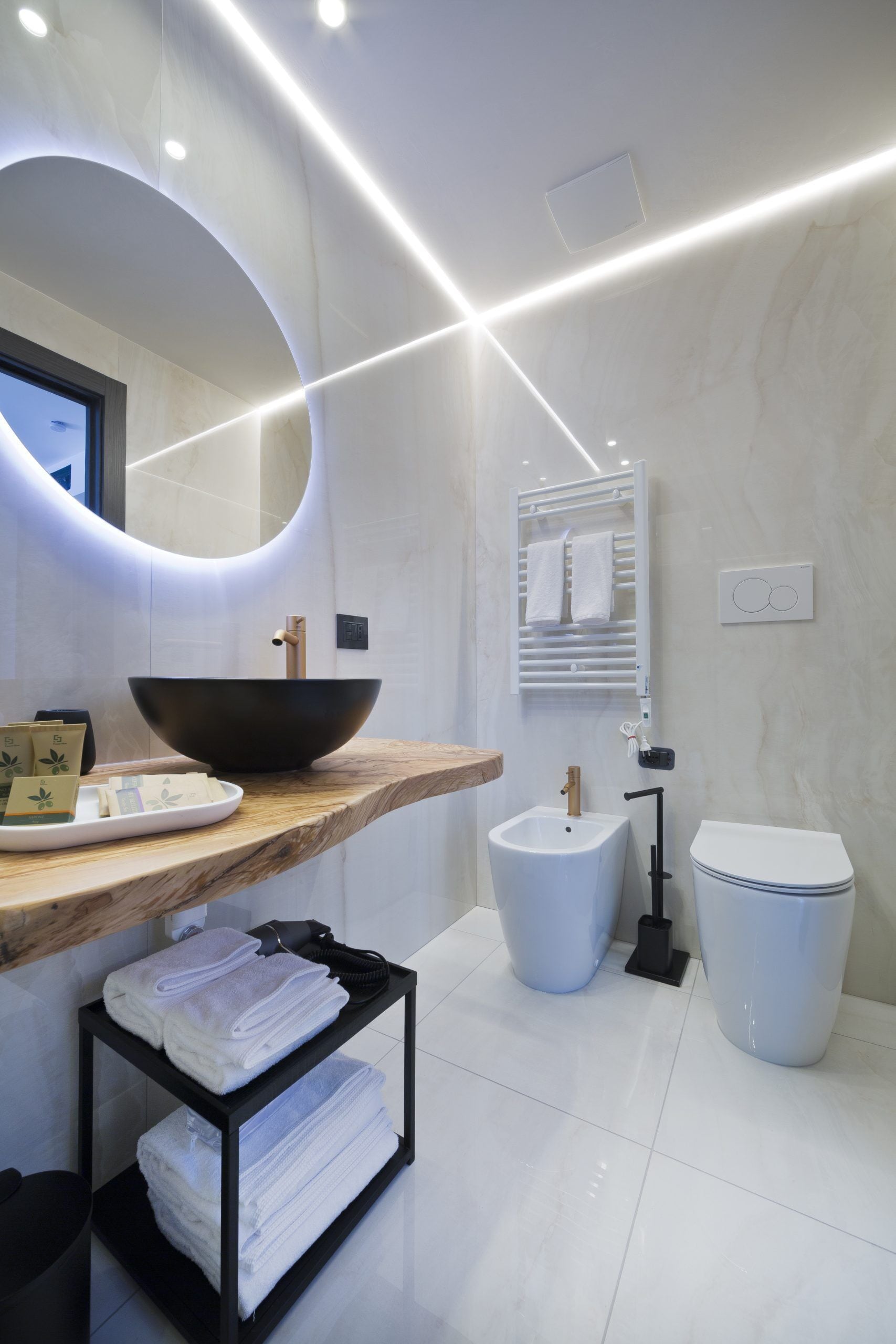 A modern bathroom with a wooden vanity, a large mirror, a black vessel sink, a bidet, and a toilet.