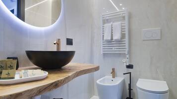 A modern bathroom with a wooden vanity, a large mirror, a black vessel sink, a bidet, and a toilet.