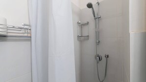Une douche équipée d’un pommeau de douche à main et d’un robinet mural, ainsi que d’un porte-serviettes et d’une étagère pour les produits de douche.