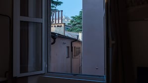 Une pièce avec une fenêtre donnant sur une rue étroite bordée d’immeubles et d’arbres.