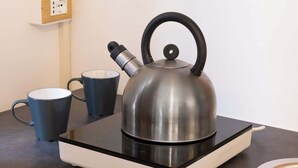 Une bouilloire sur une plaque de cuisson à induction noire, avec deux tasses à côté.