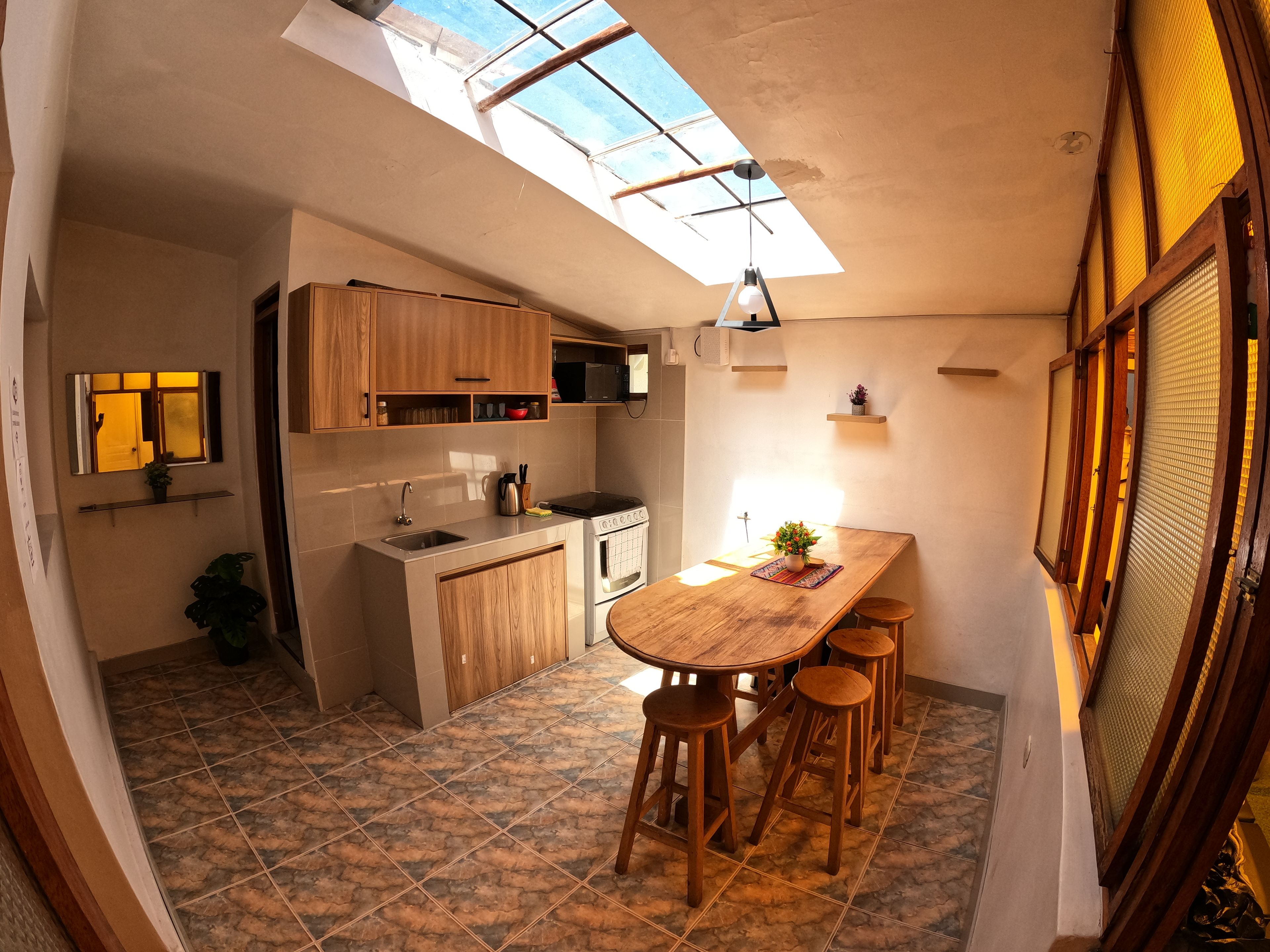 A compact kitchen with a skylight, wooden cabinets, a central island with stools, and a tiled floor.
