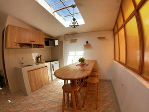 A kitchen with wooden cabinets, a stove, and a dining area with a table and stools. - Ekeko's Apartment - Calle Matara (Cusco)