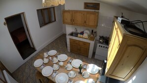 A compact kitchen with wooden cabinets, a stove, and a dining area set for a meal. - Ekeko's Apartment - Calle Matara (Cusco)
