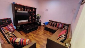 A living room with a flat-screen TV, wooden flooring, two sofas with colorful cushions, and a small table with decorative items. - Ekeko's Apartment - Calle Matara (Cusco)
