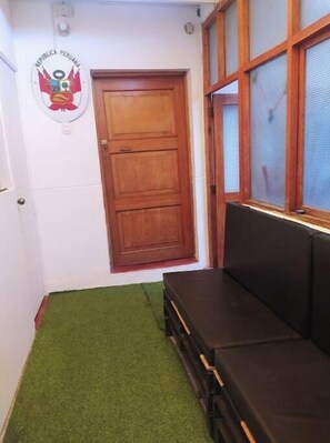 Un pasillo estrecho con una puerta de madera, un emblema en la pared y una ventana con persianas.
