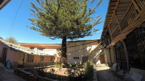 A courtyard with a large tree, a building with a tiled roof, and a metal gate. - Ekeko's Apartment - Calle Matara (Cusco)