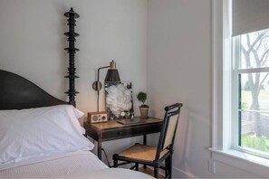 Une chambre à coucher avec un lit, un bureau avec une lampe, une chaise et une fenêtre.