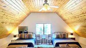 Una camera da letto mansardata accogliente con due letti, una ventola a soffitto e una finestra che fa entrare luce naturale.