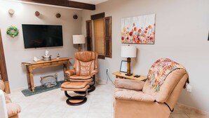 A living room with a leather recliner, a sofa, a wooden desk, and a flat-screen TV mounted on the wall.
