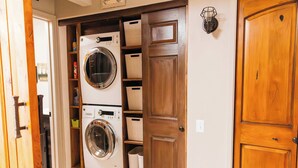 A laundry room with a front-loading washer and dryer, wooden shelving with baskets, and a wooden door.