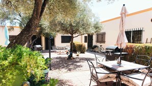 An outdoor patio with a table and chairs, surrounded by greenery and a tree.