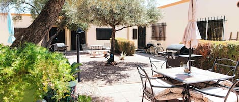 An outdoor patio with a table and chairs, surrounded by greenery and a tree.