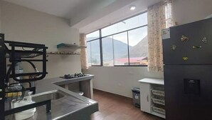 A kitchen with a gas stove, a sink, a refrigerator, and a window with a mountain view. - Casita de Diego (Calca)