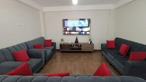 A living room with two grey sofas and red cushions, a wooden coffee table, and a flat-screen TV mounted on the wall. - Casita de Diego (Calca)