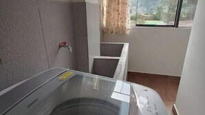 A laundry room with a large washing machine, a dryer, and a window with a view of mountains. - Casita de Diego (Calca)