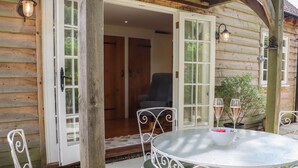 Eine Holzhütte mit einer Terrasse, auf der ein runder Tisch und Stühle stehen und ein Glas Champagner steht.
