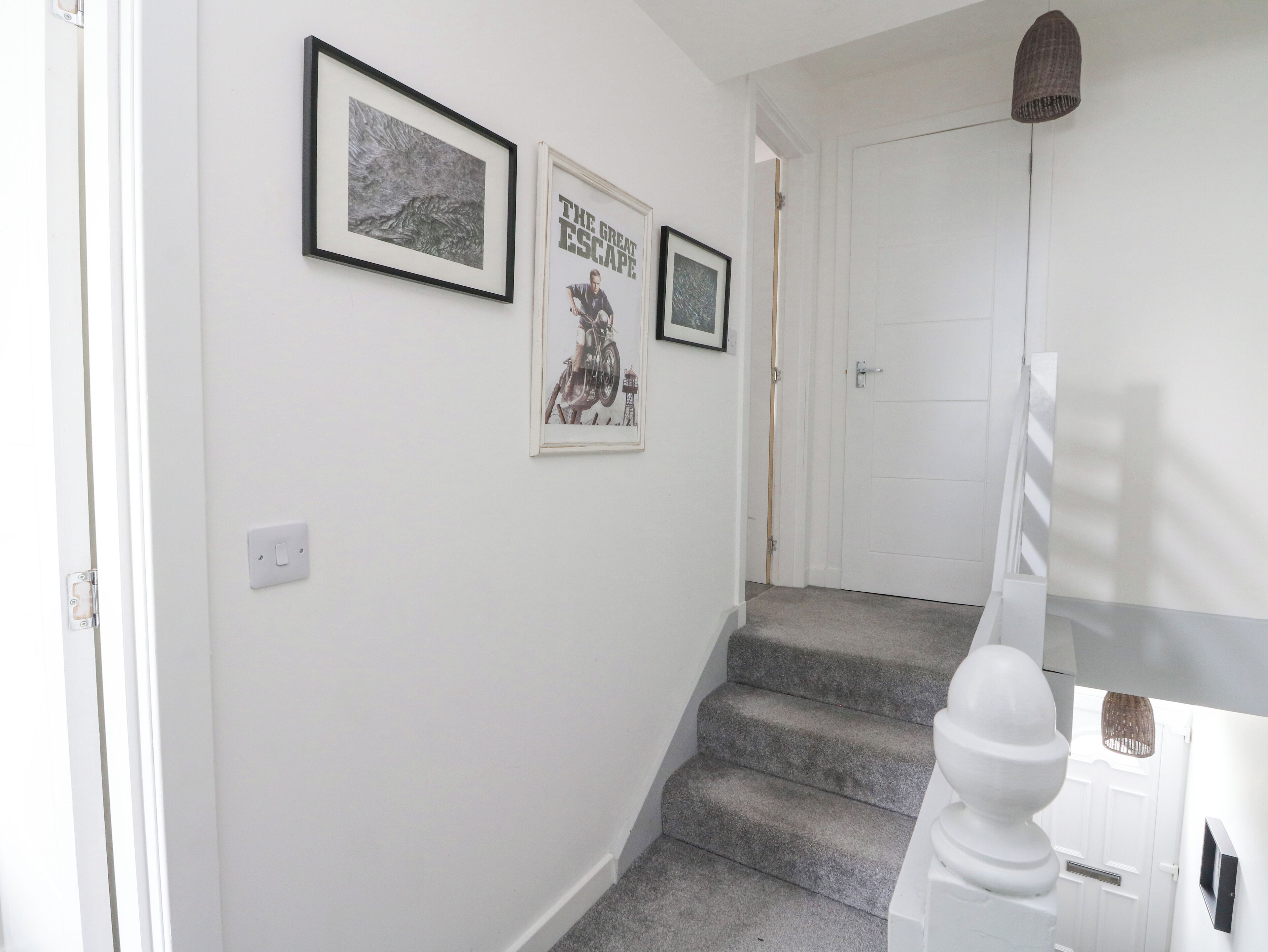 Un escalier avec une rampe blanche, une porte en haut et deux tableaux encadrés accrochés au mur.