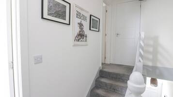 Un escalier avec une rampe blanche, une porte en haut et deux tableaux encadrés accrochés au mur.