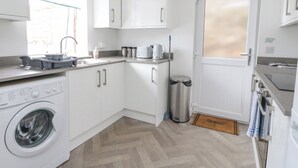 A compact kitchen with white cabinets, a washing machine, a sink, and a door with a window. - Anchor Cottage (Elgin)