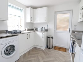 A compact kitchen with white cabinets, a washing machine, a sink, and a door with a window.
