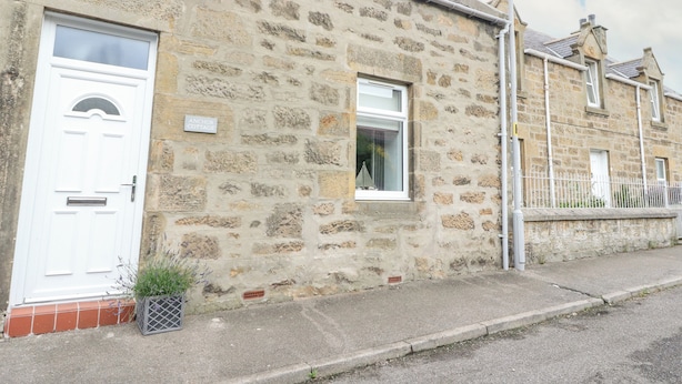 A stone cottage with a white door, a small window, and a nameplate reading "Anchor Cottage". - Anchor Cottage (Elgin)