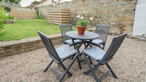 A patio with a round table and four chairs, surrounded by a stone wall and a grassy area with trees. - Anchor Cottage (Elgin)