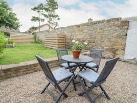 A patio with a round table and four chairs, surrounded by a stone wall and a grassy area with trees.