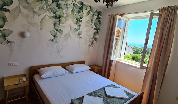 Un dormitorio con cama, mesita de noche, ventana con cortinas y un papel tapiz con diseño de hojas.