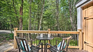 Une terrasse dotée d’une table et de chaises, entourée d’une rambarde en bois, et offrant une vue sur une zone boisée.