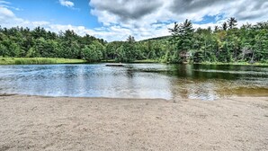 Un paysage paisible au bord d’un lac, avec une plage de sable, une forêt dense et une jetée qui s’avance dans l’eau.