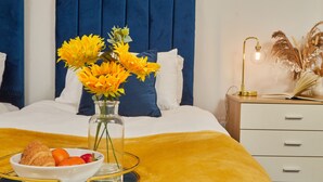 A neatly made bed with a blue headboard, a bedside table with a lamp, and a bowl of breakfast including croissants, oranges, and strawberries. - Sleeps 3: Family & Work Stays - FREE Parking & WiFi (Woodhouse)