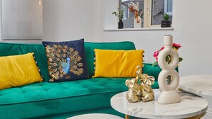 A green sofa with colorful cushions, a white vase with a flower, and a decorative sculpture on a round table. - Sleeps 3: Family & Work Stays - FREE Parking & WiFi (Woodhouse)