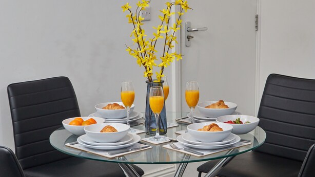 A breakfast table with croissants, orange juice, and a vase with yellow flowers. - Sleeps 3: Family & Work Stays - FREE Parking & WiFi (Woodhouse)