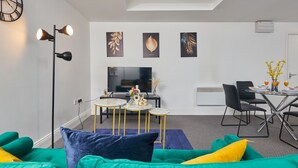 A modern living room with a green sofa, a dining table with chairs, a flat-screen TV, and a ceiling light fixture. - Sleeps 3: Family & Work Stays - FREE Parking & WiFi (Woodhouse)