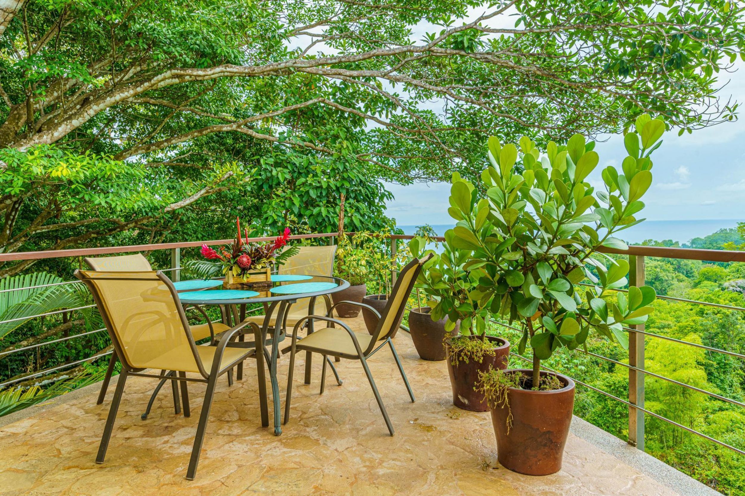 An outdoor patio with a table and chairs, surrounded by potted plants and overlooking a lush landscape.