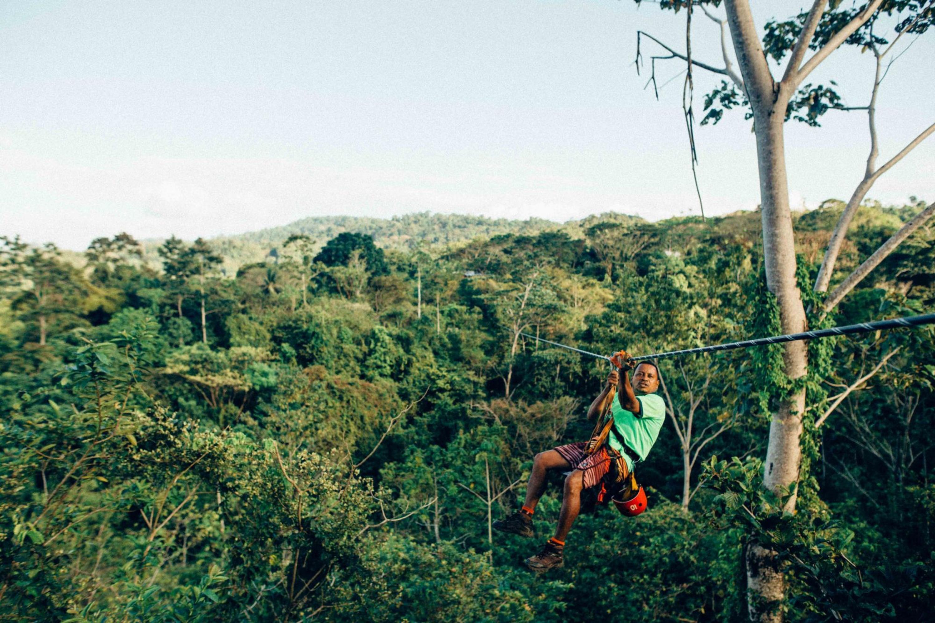A person suspended on a zip line in a forested area.