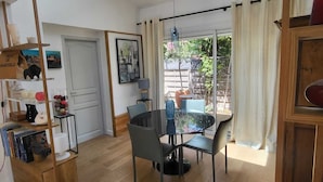 Uma sala de jantar com uma mesa redonda e cadeiras, uma estante, uma porta e uma janela com cortinas.