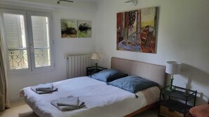 Quarto com cama, duas mesas de cabeceira, radiador e janela com persianas.