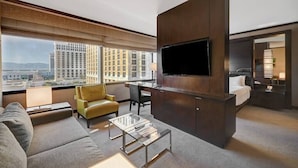 Habitación de hotel moderna con un televisor grande, un sofá, una mesita de centro y vistas a la ciudad.