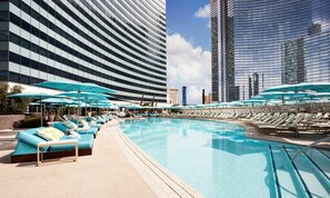 A poolside area with lounge chairs and umbrellas, surrounded by modern high-rise buildings.