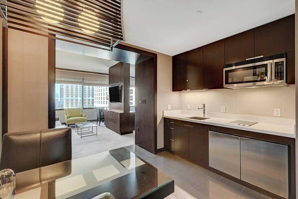 A modern kitchen with dark cabinetry, a stainless steel microwave, and a glass dining table.