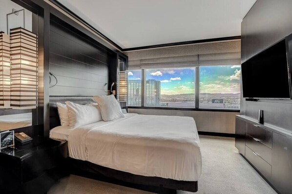 A modern hotel room with a large bed, a TV, and a city view.
