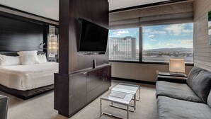 Une chambre d’hôtel moderne équipée d’un lit, d’une télévision, d’un canapé et d’une grande fenêtre donnant sur la ville.