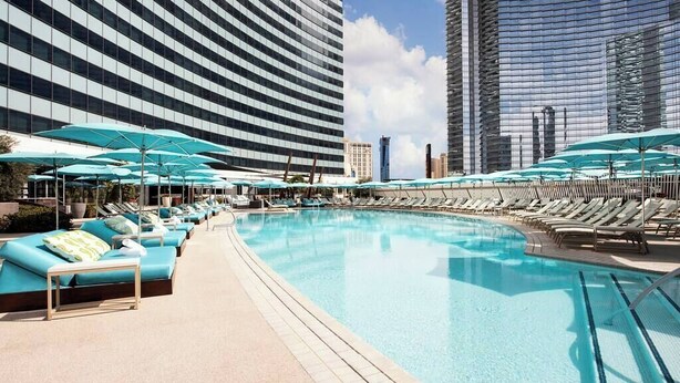 Ein moderner Hotelpoolbereich mit Liegestühlen und Sonnenschirmen, umgeben von Hochhäusern.