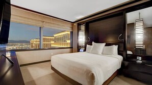 A modern hotel room with a large bed, a desk, and a view of a cityscape at night.