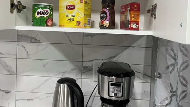 Una cocina con cafetera, hervidor y un estante con diversos productos alimenticios.